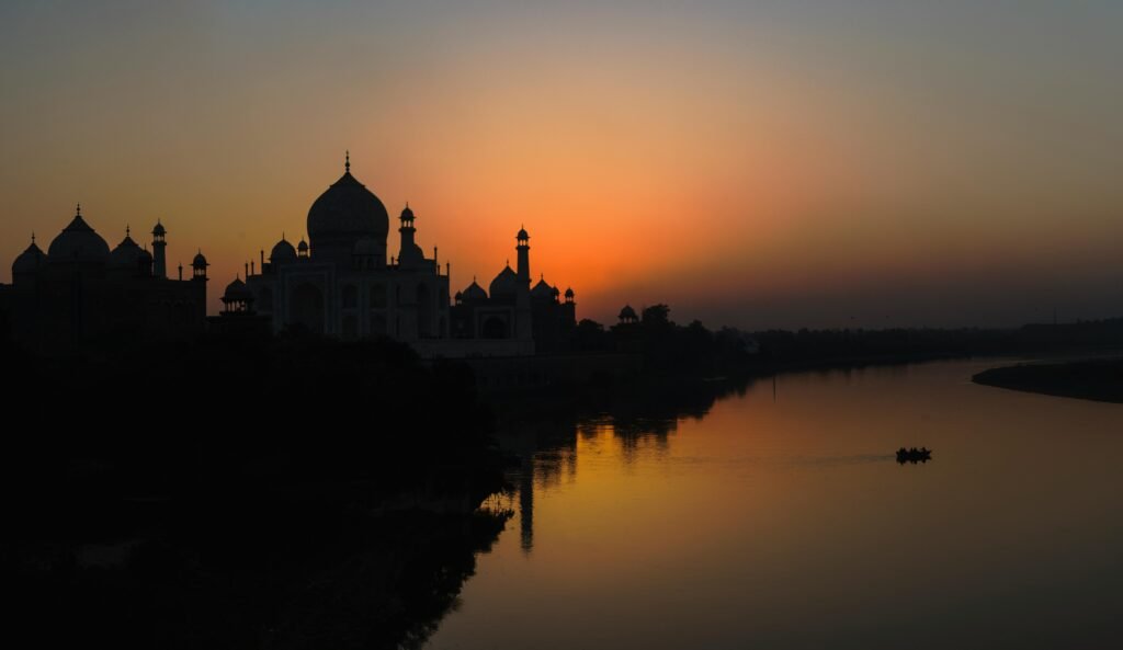A stunning silhouette of the Taj Mahal at sunset along the Yamuna River, showcasing architectural beauty.