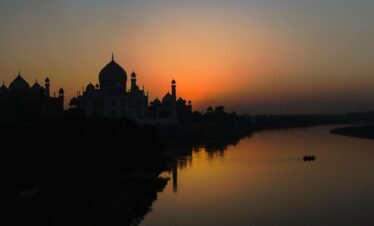 A stunning silhouette of the Taj Mahal at sunset along the Yamuna River, showcasing architectural beauty.