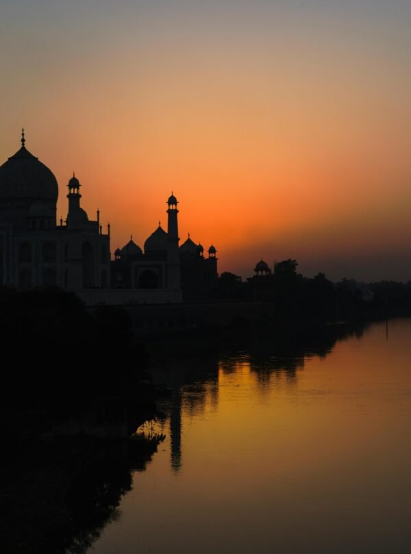 A stunning silhouette of the Taj Mahal at sunset along the Yamuna River, showcasing architectural beauty.