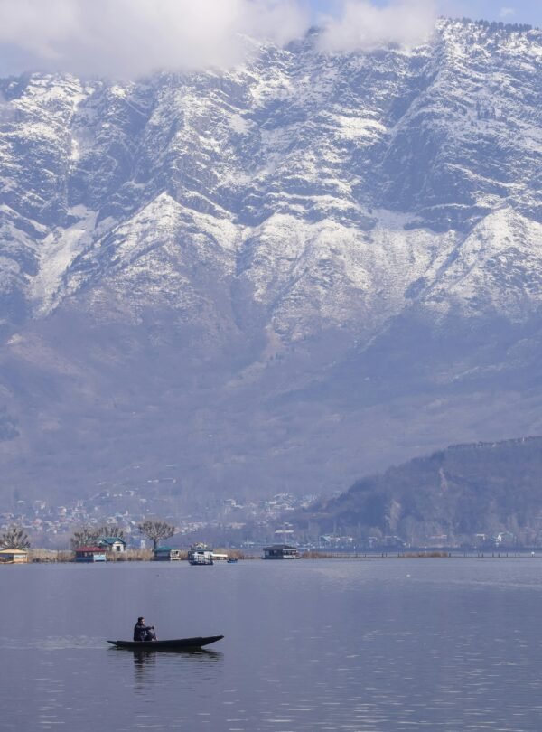 Tranquil scene of a boat on Dal Lake with snow-capped Zabarwan mountains in Srinagar.
