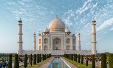 Front view of the Taj Mahal, showcasing its iconic architecture against a blue sky.