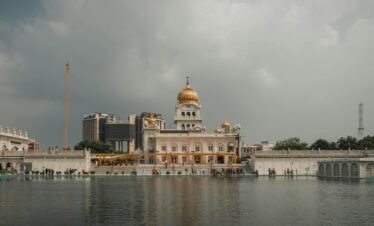 Stunning view of Gurudwara Bangla Sahib with reflection on the water under a cloudy sky in Delhi.