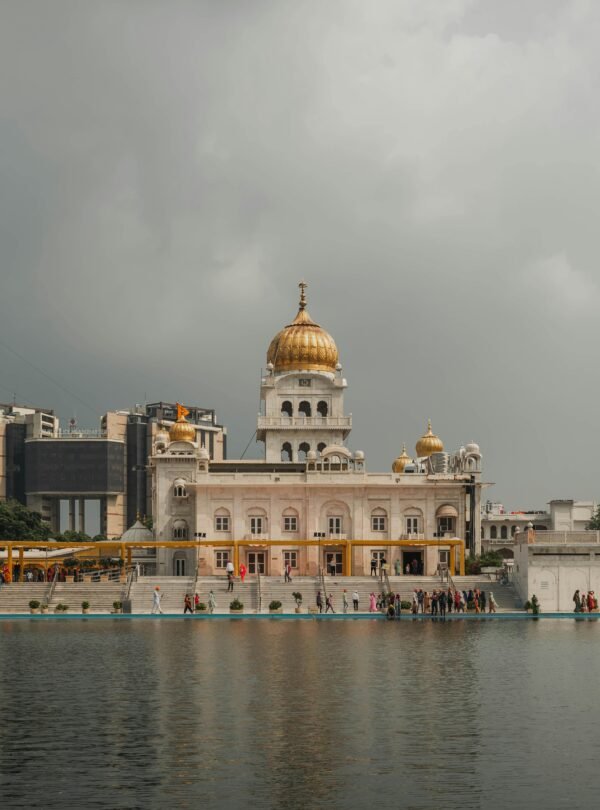 Stunning view of Gurudwara Bangla Sahib with reflection on the water under a cloudy sky in Delhi.